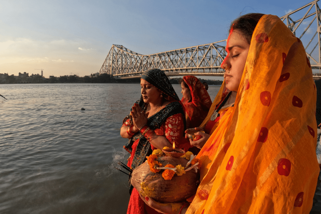Women performing Chhath Puja rituals at river ghat, showing regional spread and evolving traditions
